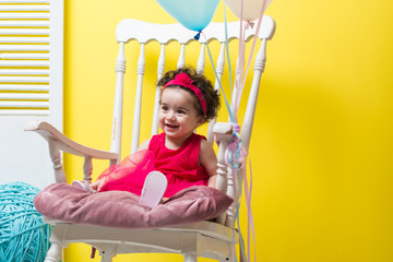 Fototapeta na wymiar Happy smiling sweet baby girl sitting on armchair with birthday balloons
