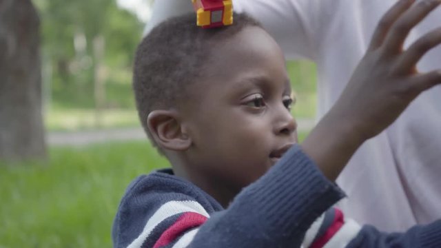 Portrait positive African American woman playing with her little son using plastic toy in the park. The young mother spending time with her child outdoors. Loving family on the picnic. Summertime