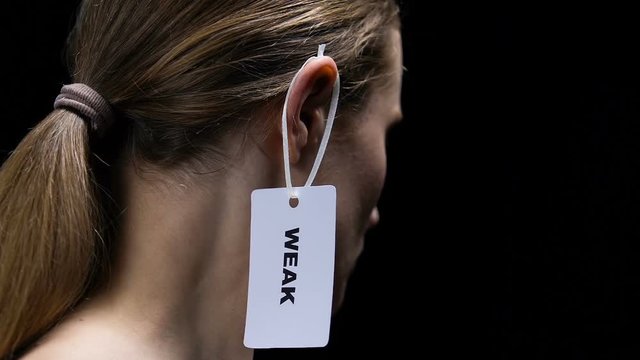 Male hand hanging weak label on female ear, underscoring personal qualities