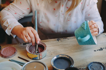 Fototapeta na wymiar Woman working In her pottery studio. Ceramic workshop. Paint on clay cup in the pottery. Painting in pottery