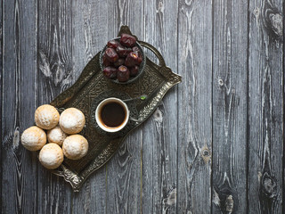 Top view on silver plate with sweets, date fruits and coffee cup on the dark wooden table. Ramadan background