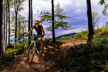 Naklejka na ściany i meble Mountain biking woman riding on bike in summer mountains forest landscape. Woman cycling MTB flow trail track. Outdoor sport activity.