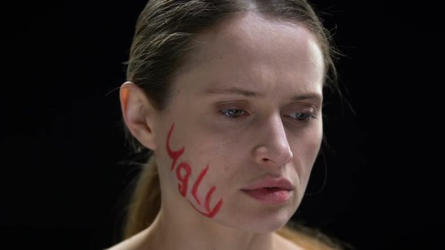 Unhappy lady turning head, ugly word written on face, suffering insecurities