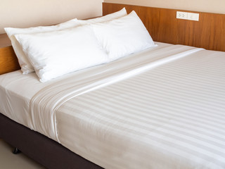 Fototapeta na wymiar Clean white bedding with four white pillows in hotel bedroom
