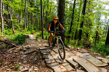 Naklejka premium Mountain biking woman riding on bike in summer mountains forest landscape. Woman cycling MTB flow trail track. Outdoor sport activity.