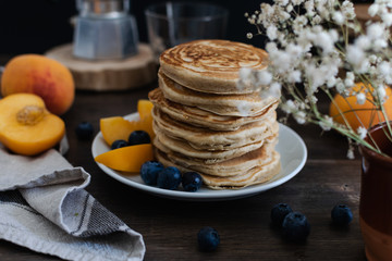 Beautiful rustic breakfast - pancakes with blueberries, peach, Gypsophila flowers, moka coffee machine, wooden table