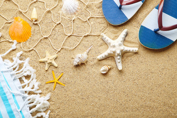 Seashells with flip flops and fishing net on beach sand