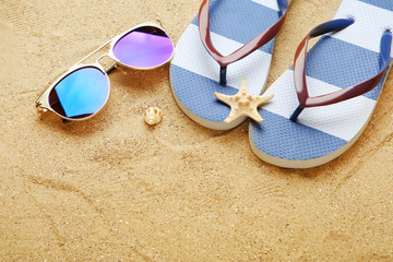 Fototapeta na wymiar Seashells with sunglasses and flip flops on beach sand
