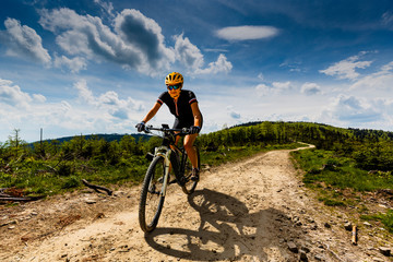 Naklejka na ściany i meble Mountain biking woman riding on bike in summer mountains forest landscape. Woman cycling MTB flow trail track. Outdoor sport activity.