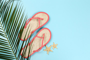 Pair of flip flops with starfishes and palm leaf on blue background