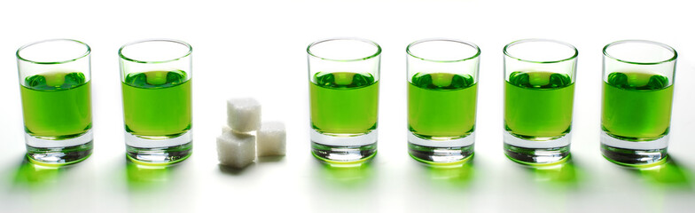 Absinthe green liquor in glasses. Alcoholic hallucinogenic beverage. White background. Pieces of white sugar.
