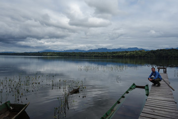Backpacker in front of a secret lake with a lot of water plants and piranhas and water reflections of the blue, cloudy sky in the Madidi Jungle, Bolivia