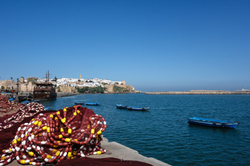 Bay with parked boats. Marina promenade with some piles of fishing nets. Walls of the kasbah in the background. Blue sky. Rabat, Morocco.
