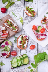 Bruschetta assortment with cream cheese, champignons, pancetta meat, vegetables and greenery against the white wooden background