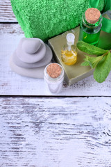 Spa set: massage stones, aromatic oil, sea salt, green gel, organic soap and green towel on white wooden table