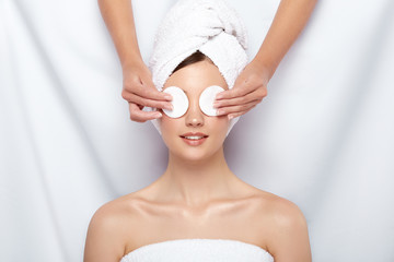 beautician closing woman's eyes with two cotton pads