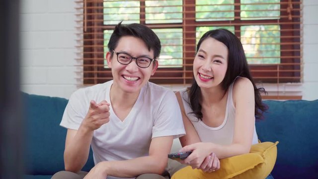 Asian couple watching television in living room at home, sweet couple enjoy love moment while lying on the sofa when relaxed at home. Lifestyle couple relax at home concept.