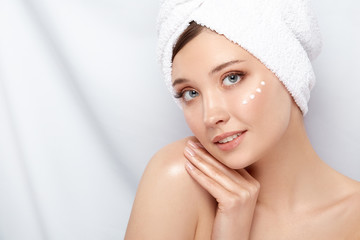 attractive girl with towel on her head touching her shoulder and having cream under her face, copy space, close-up