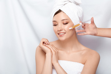 beautician holding syringe near woman's face in bath towel and open shoulders, woman getting beauty injection isolated on white