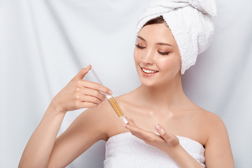 pretty woman in bath towel on her head holding beauty injection and looking on it with smile, face...