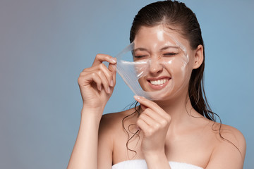 happy woman removing with hardness her facial mask and smiling, pretty young girl doing spa procedures, copy space