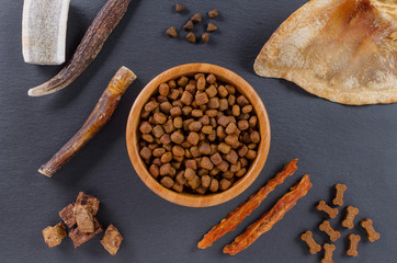 different dog food and snack, chicken filet, antlers, lung, ear on black background, top view