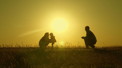 mother and Dad play with their daughter in sun. happy baby goes from dad to mom. young family in the field with a child 1 year. family happiness concept. beautiful sunshine, sunset.