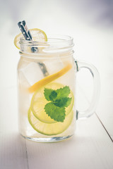 Lemonade Cocktail Mojito with Fresh Cold Ice, Lemon and Mint Leaves in Mason Jar on White Wooden Background. Bright Summer Concept.