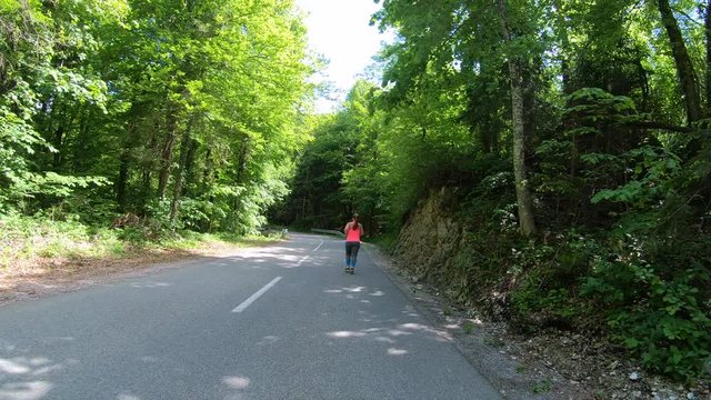 Wide forward tracking shot of an overweight woman running up a forest road on a sunny day 