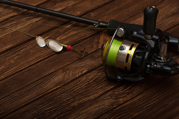 Spinning with a reel on an old brown wooden background. Metal Fishing lure. Beautiful relief boards. Carbon rod. Fishing. Summer. Place for text.