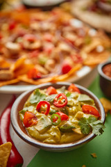 Close up on guacamole dip in bowl with various freshly made Mexican foods