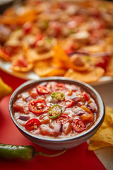 Close up on hot tomato dip in ceramic bowl with various freshly made Mexican foods