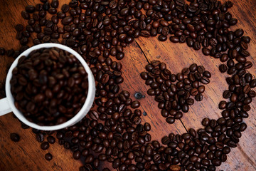 Image of cup full of coffee beans with heart shape from coffee beans on wooden background