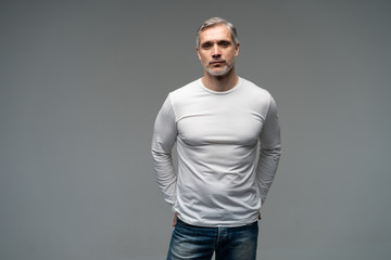Cheerful man of middle age against gray background, wearing jeans and white T-shirt, mid shot.
