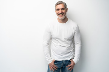 Cheerful man of middle age against white background, wearing jeans and white T-shirt, mid shot.