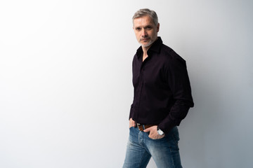 Fototapeta premium Cheerful man of middle age against white background, wearing jeans and black shirt, mid shot.