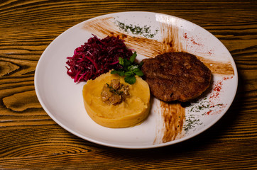closeup two pieces of medium raw grilled meat decorated with red pepper and sauce served with potato chips and vegetable salad on black restaurant plate on wooden table.