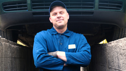 A cheerful car repairman on the street repairs the engine and lower part of the car, shows different emotions, dances with a big wrench. Concept of: Service, Joy, Slow motion, Mood, Happy, Repair.