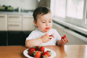 Little girl child in white t-shirt eating strawberries all smeared and dirty