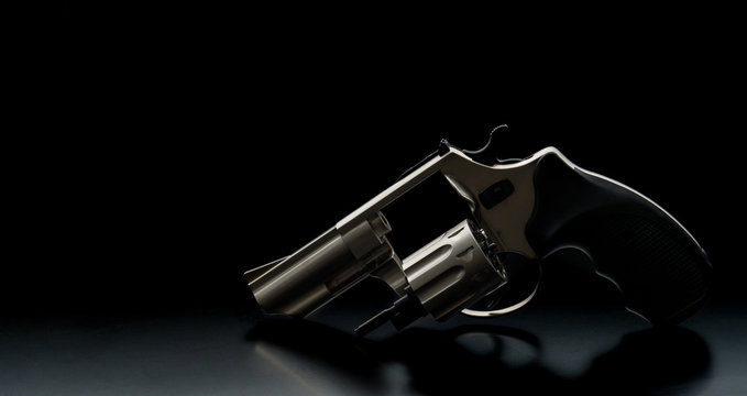 Silver pistol revolver on a black back. Low key photography. Weapon concept. Background for gun postcard.