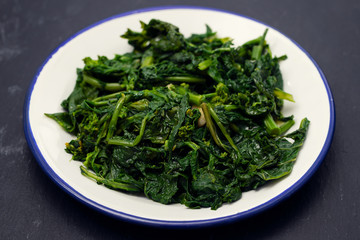 boiled greens with garlic on white plate on black ceramic background
