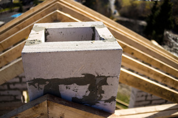 Close-up detail of roof frame of rough wooden lumber beams and chimney made of foam insulation blocks on blurred green background. Building, roofing, construction and renovation concept.