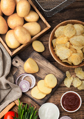 Fresh organic homemade potato crisps chips in wooden bowl with sour cream and red onions and spices on wooden table background. Top view.Fresh yellow potatoes with ketchup