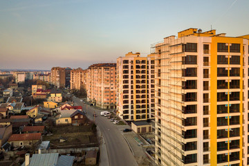 Row of tall apartment buildings and unfinished building with scaffolding along road with parked cars on blue sky copy space background. Aerial view.