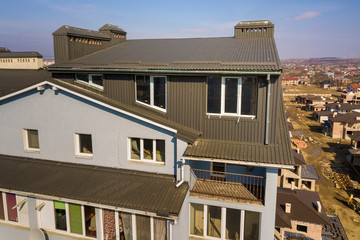 Obraz na płótnie Canvas Aerial view of attic annex room exterior with plastic windows, roof and walls covered with brown metal decorative siding planks, new gutter system on top of apartment building.