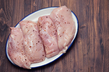 raw chicken breasts on white dish on brown wooden background