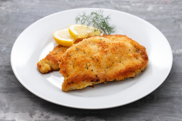 fried chicken with lemon on white plate on ceramic background