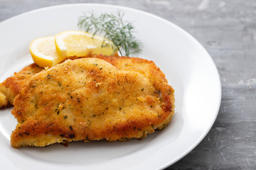 fried chicken with lemon on white plate on ceramic background