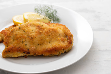 fried chicken with lemon on white plate on ceramic background