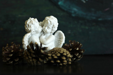 White statuette of two angels kissing each other decorated by pine cones